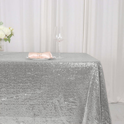 Silver sequin tablecloth draped elegantly on a table with floral centerpiece and glass.