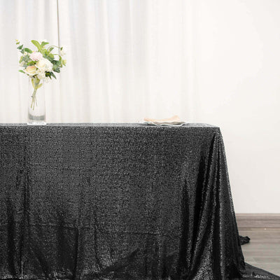 Black sequin tablecloth with a vase of flowers and plates on a table.