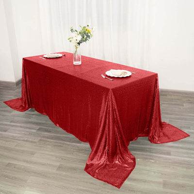 Red sequin tablecloth draped over a dining table with plates and a vase of flowers.