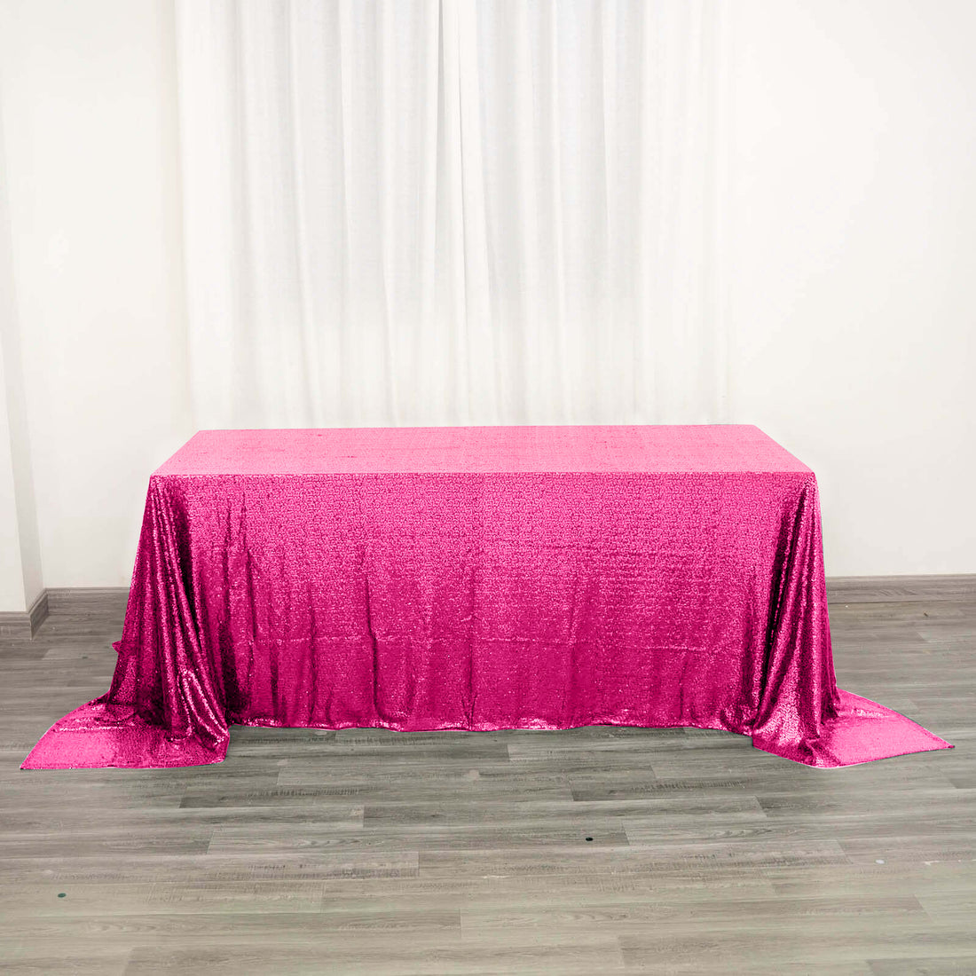 Pink sequined tablecloth on a wooden floor with white curtains.