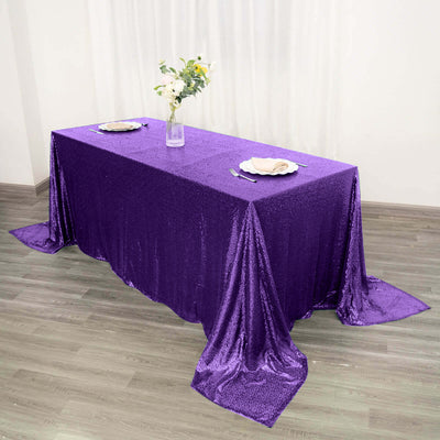 Purple sequin tablecloth draped over a table with plates and flowers.