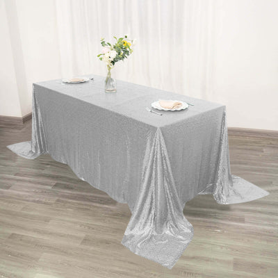 Silver sequin tablecloth draped over a rectangular table with plates and flowers.