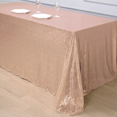 Rose gold sequin tablecloth draped over a table with glasses and plates.