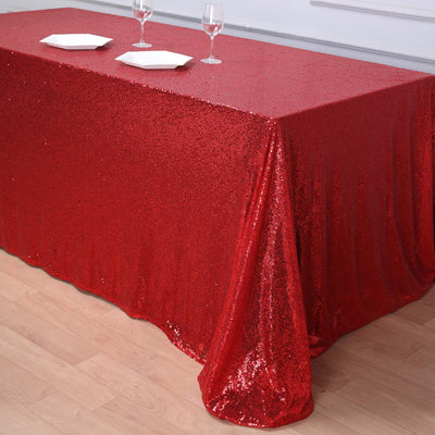 Red sequin tablecloth draped on a wooden table with glassware and plates.