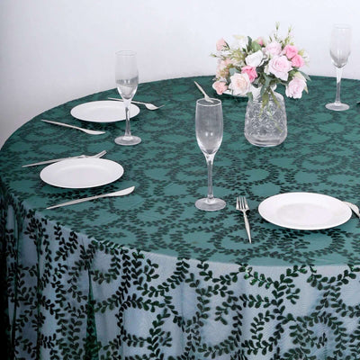 Round table set with green leaf-patterned tablecloth and elegant glassware.