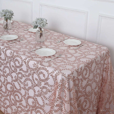 Rose gold patterned tablecloth on a dining table with plates and floral centerpieces.