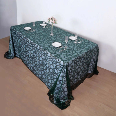 Elegant green lace tablecloth draped over a dining table with plates and glasses.
