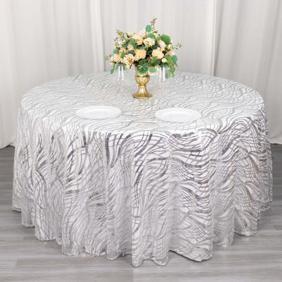 Elegant round table draped in a decorative silver swirl tablecloth with flower centerpiece.