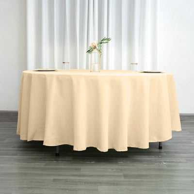 Beige round tablecloth on a table with a vase and glasses in a bright setting.