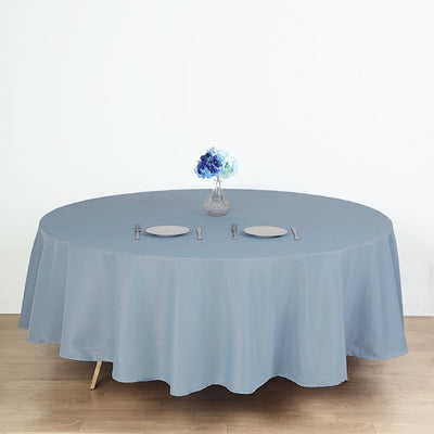 Round blue tablecloth on a dining table with plates and a vase of flowers.