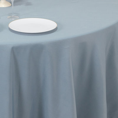 Light blue tablecloth draped over a table with a white plate and glass.