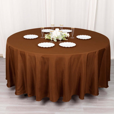Brown round tablecloth draped over a table with white plates and decorative centerpiece.