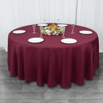 Round burgundy tablecloth draped over a table with decorative plates and flowers.