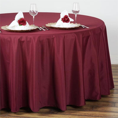 Burgundy tablecloth draped over a round table set with plates and glasses.