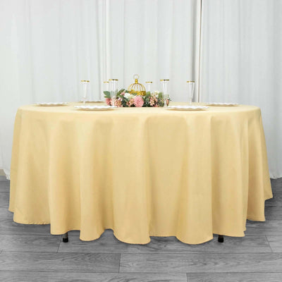 Round beige tablecloth draped over a table with floral centerpiece and glassware.