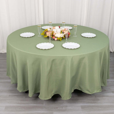 Round green tablecloth with decorative table setting and floral centerpiece.