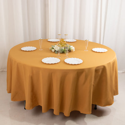 Round table set with gold tablecloth and white plates, elegantly decorated with flowers.