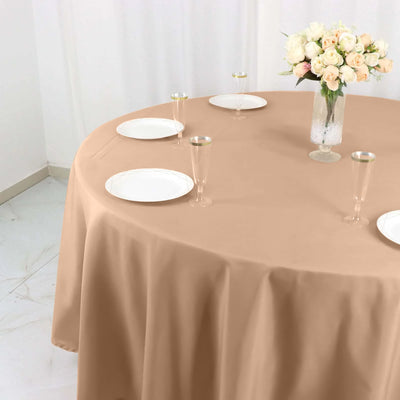 Beige tablecloth draped over a round table with plates and a floral centerpiece.