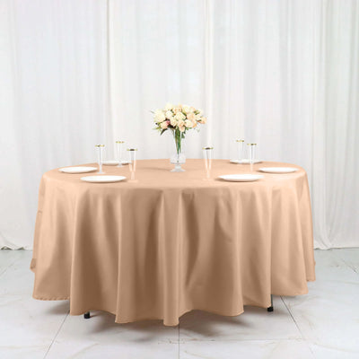 Round beige tablecloth draped over a table with plates and floral centerpiece.