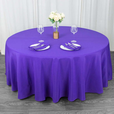 Purple round tablecloth with white plates and glasses on a table.