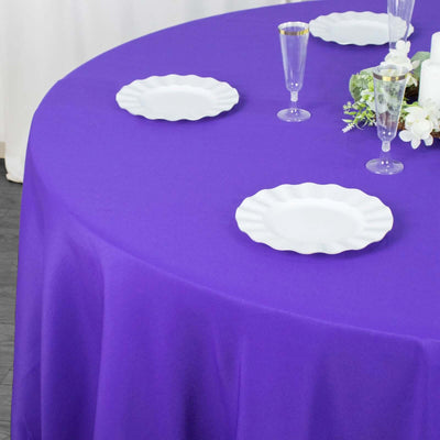 Purple tablecloth on a round table set with white plates and elegant glassware.