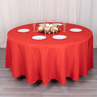 Red round tablecloth draped over a table with plates and floral centerpiece.