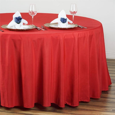 Red tablecloth draped on a round table set with napkins and glasses.