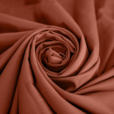 Rust-colored fabric rolled in a spiral pattern. #whtbkgd