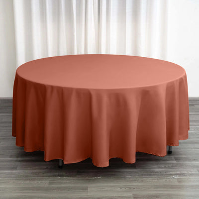 Round terracotta tablecloth on a wooden floor with curtains in the background.