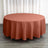 Round terracotta tablecloth on a wooden floor with curtains in the background.