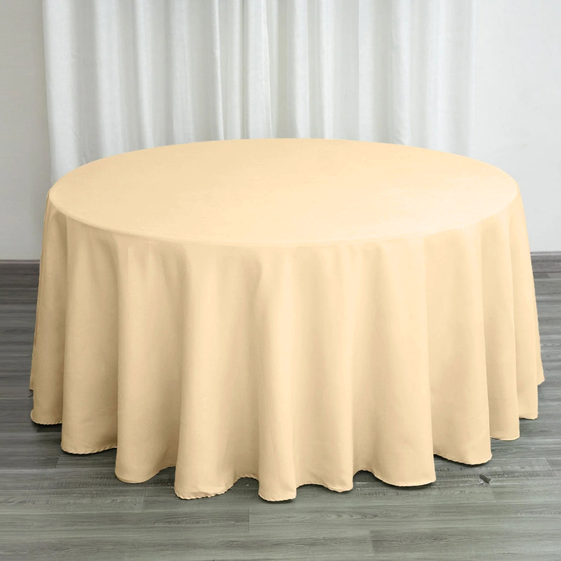 Round beige tablecloth draped over a table in a staged setting.