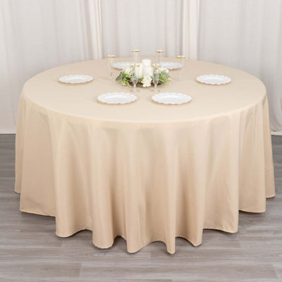 Round beige tablecloth draping a circular table with decorative plates and candles.