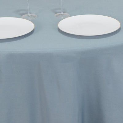 Two white plates on a blue tablecloth with glasses in the background.