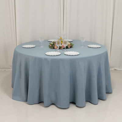 Round blue tablecloth on a dining table with white plates and floral centerpiece.
