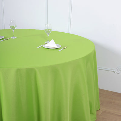 Round green tablecloth on a table set with glasses and napkins.