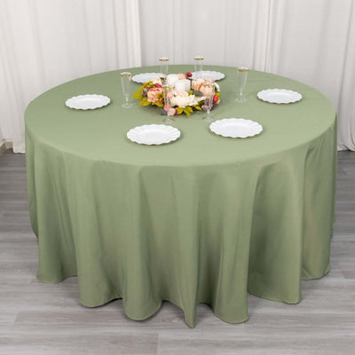 Round green tablecloth with white plates and floral centerpiece on a table.