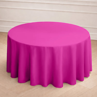 Round pink tablecloth draped over a table set with plates and glasses.