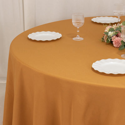 Round table with mustard tablecloth, white plates, and floral centerpiece.