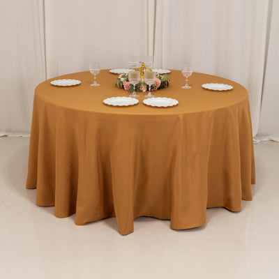 Round brown tablecloth with decorative plates and glasses set for dining.