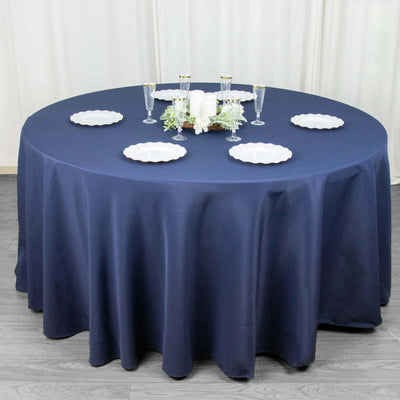 Round navy tablecloth with elegant white plates and glassware arranged for dining.