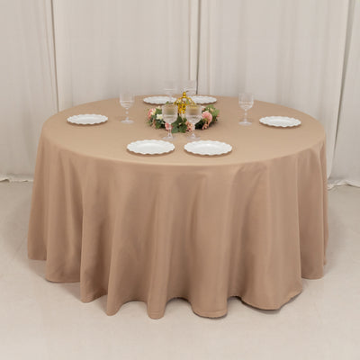Round beige tablecloth draped over a round table set for dining.