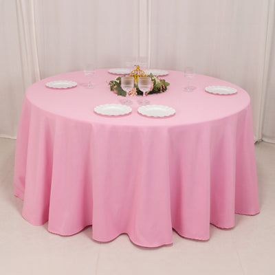 Round pink tablecloth draped over a table with white plates and glassware.