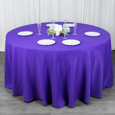 Purple round tablecloth draped over a table with white plates and glassware.
