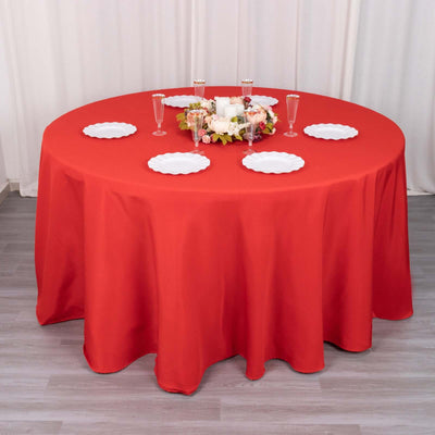 Round red tablecloth on a dining table set with plates and decor.