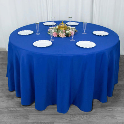 Blue round tablecloth on a table set for an event with decorative plates and flowers.