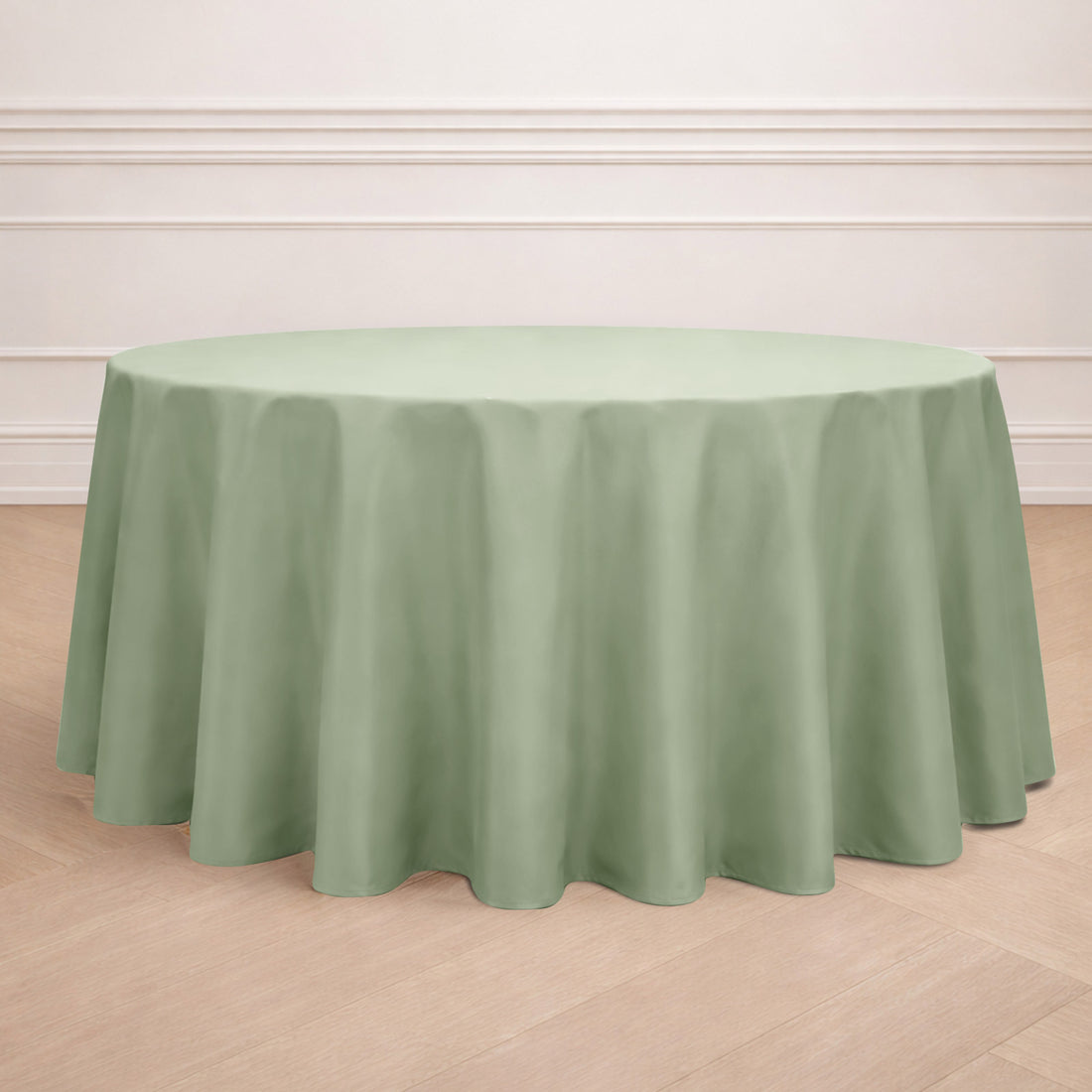 Round sage green tablecloth on a wooden floor.