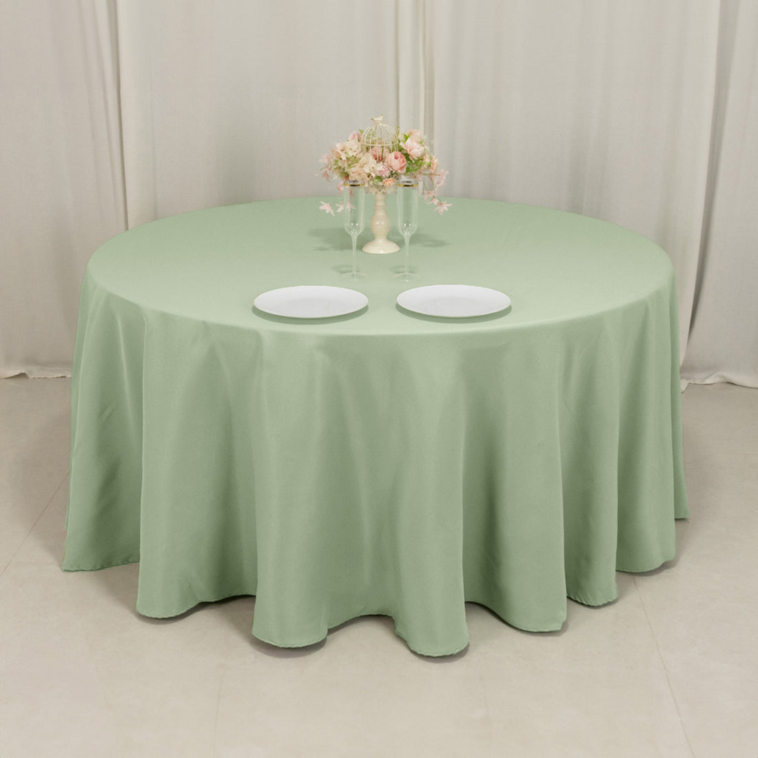 Round mint green tablecloth on a dining table with plates and a floral centerpiece.