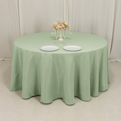 Round mint green tablecloth on a dining table with plates and a floral centerpiece.