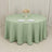 Round mint green tablecloth on a dining table with plates and a floral centerpiece.