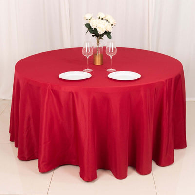 Round red tablecloth with white plates and glasses on a decorated table.